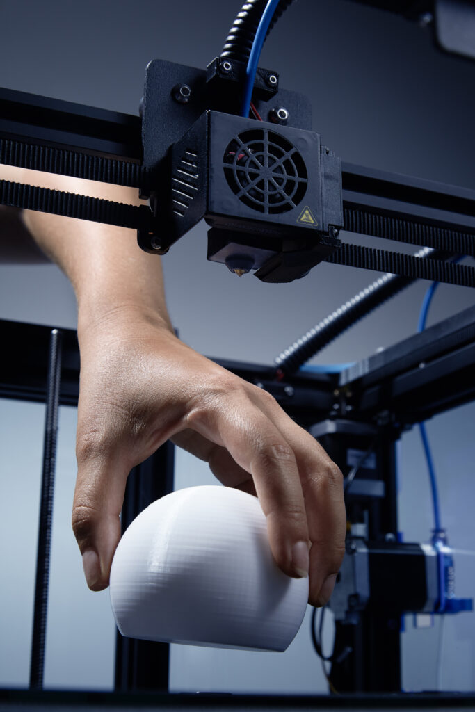 3D printer finish prototype print. Hand picking up printed white object. Fan, wires, tech ambient. Vertical high quality studio up view studio photo image. Genderneutral Hand Lifting Up From Structure 3d Printed Round Object Made From Recycled Plastic Futuristic Concept New Working Possibilities Small Businesses By 3d Printing Jpg Photo 683x1024